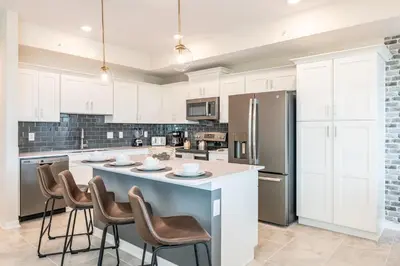 a kitchen with white cabinets and a large island with bar stools at Chic 2Bed Condo at Storey Lake Mickey Room in Kissimmee