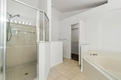 a white bathroom with a shower and a tub at Luxury 4-Bedroom Home with Private Pool, Jacuzzi, AC, Wi-Fi, Cable TV, 5 Minutes from Disney in Kissimmee