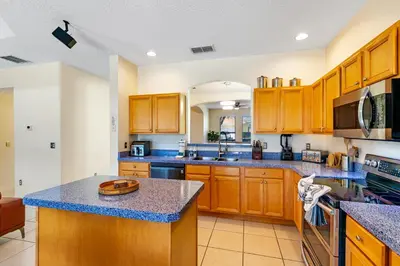 a large kitchen with wooden cabinets and blue granite counter tops at Luxury Emerald Island Resort Villa with Stunning Pool Deck and Lake View Near Disney in Kissimmee