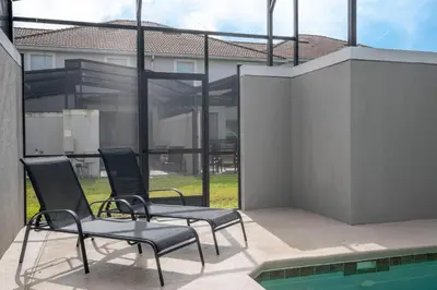 two chairs sitting on a patio next to a swimming pool at 4812 BR - Enchanted Lakeside Escape Luxurious Family Retreat in Kissimmee