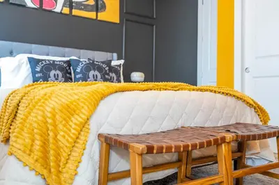 a bed with a yellow blanket and a wooden bench at The Mouse PlayHouse in Orlando