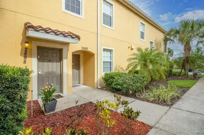 a yellow house with a gray door and some bushes at Oakwater Resort Home w/ Arcade & Pool Table - 15 Min to Disney in Orlando