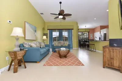 a living room with a blue couch and a kitchen at Caribbean Breeze: Pool Home 3 Miles to Disney in Kissimmee