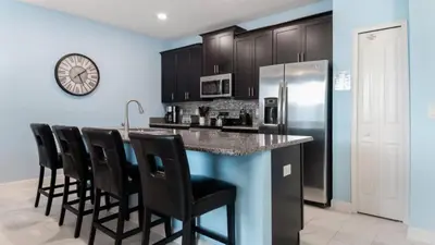 a kitchen with a bar with black chairs and a refrigerator at Gatsby Escape: Private Pool Near Disney & Resorts in Kissimmee