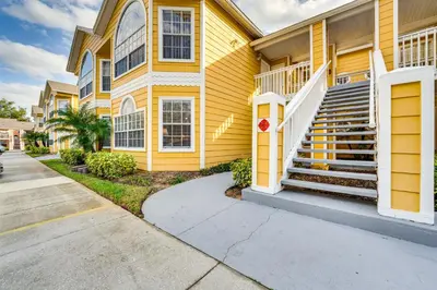 a yellow house with stairs on a street at 7 Mi to Disney Condo with Pool and Hot Tub Access! in Kissimmee