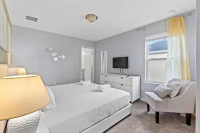 a white bedroom with a bed and a chair at Compass Bay: 4Q reformados Perto da Disney! in Kissimmee