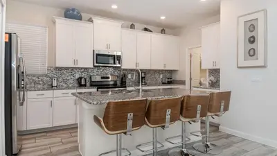a kitchen with white cabinets and a island with bar stools at KCC 4797 in Kissimmee