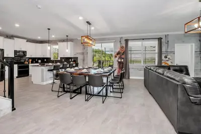 a woman standing in a kitchen with a table and chairs at Brand New Storey Lake 8BR Villa with Lake View in Kissimmee