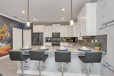 a kitchen with white cabinets and a large island with chairs at Brand New Storey Lake 8BR Villa with Lake View in Kissimmee