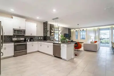 a large kitchen with white cabinets and a living room at FLASH SALE Pvt Pool and Spa Home at Storey Lake in Kissimmee