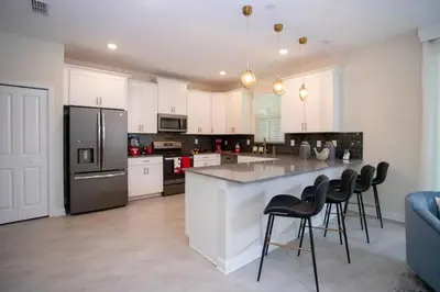 a kitchen with white cabinets and a large island with bar chairs at Casa 6Q de Alto Padrão c/ Game Room & Piscina in Kissimmee