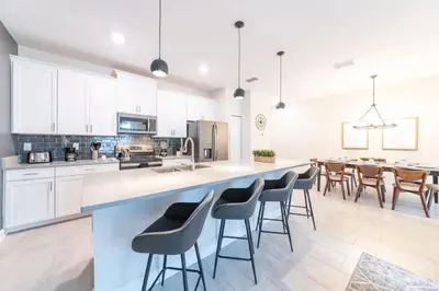 a kitchen with white cabinets and a large island with bar stools at Casa 4Q com Piscina Privativa Próxima à Disney in Kissimmee