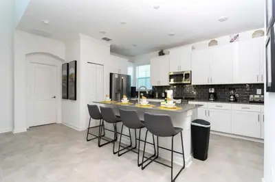a kitchen with white cabinets and a island with bar stools at Casa 5Q Storey Lake – Resort & Piscina in Kissimmee