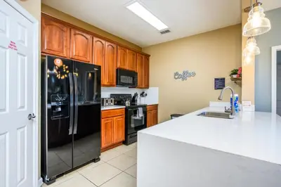 a kitchen with a black refrigerator and wooden cabinets at Beautiful Modern Condo, Near the Parks! - 3021 in Orlando