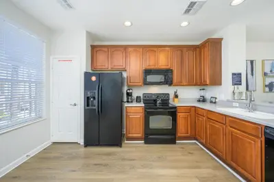 a kitchen with wooden cabinets and a black refrigerator at Epic Universe New Listing, Family Vacation Townhome - 4011 in Orlando