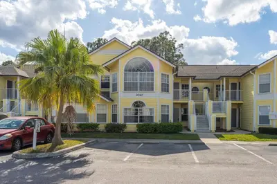 a yellow house with a palm tree in a parking lot at Disney-Area Kissimmee 3BR | Community Pool in Kissimmee