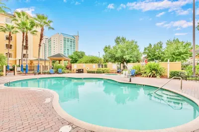 a large swimming pool with blue chairs and trees at Condo w Pool & Hot Tub - Close to Universal Studio in Orlando