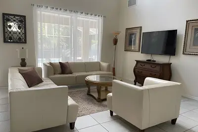 a living room with white furniture and a flat screen tv at Emerald Island Resort : Pool & Games Room in Kissimmee