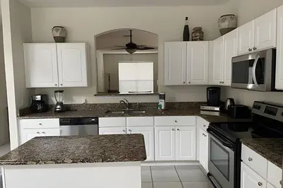a kitchen with white cabinets and a granite counter top at Emerald Island Resort : Pool & Games Room in Kissimmee