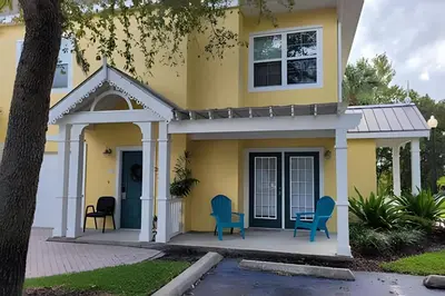a yellow house with blue chairs on a porch at Runaway Beach Club Condo near Disney in Kissimmee