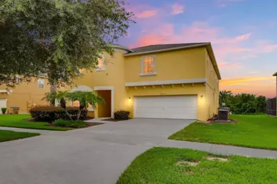 a large yellow house with a garage at Lakefront 6BR Resort Pool Home Near Disney World in Kissimmee