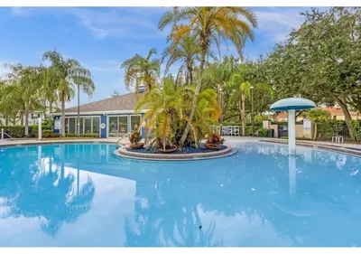 a large swimming pool with palm trees in front of a building at Amazing 4 bdr house near Disney 16101 in Kissimmee