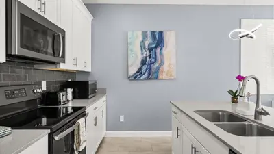 a kitchen with white cabinets and a sink and a painting at Summer in Style - 4 BR TownHome with Private pool in Kissimmee