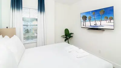 a white bedroom with a white bed and a flat screen tv at Caribbean Summer - Serene Patio in Orlando