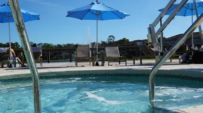 a swimming pool with an umbrella and chairs and tables at Orlando's Heartland with Amenities in Kissimmee