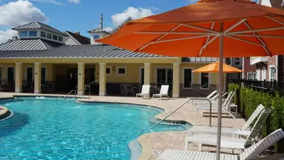 a pool with an orange umbrella and chairs and a house at Sunrise in Kissimmee - Near Disney World in Orlando