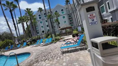 a woman sitting in a lawn chair next to a swimming pool at 110 - Next to Disney - Pool in Orlando