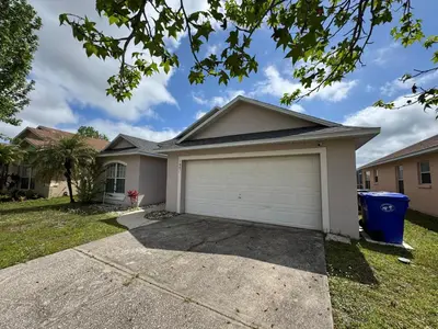 a house with a garage in a yard at Relaxing 3BR/2BA Home - Just 15 Minutes from Disney! in Kissimmee