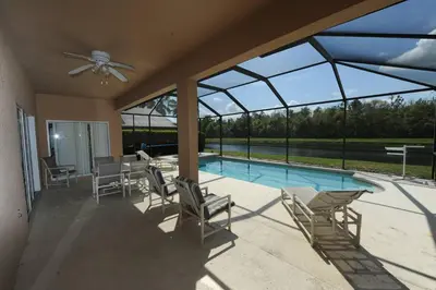 a patio with chairs and a swimming pool with windows at Tranquil Waters Haven in Kissimmee