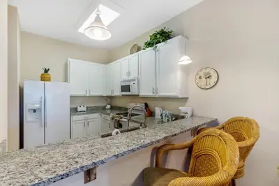 a kitchen with white cabinets and a counter with two chairs at Three-Bedroom Apartment Kissimmee in Orlando