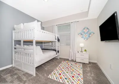 a white bedroom with a bunk bed and a tv at Disney Getaway Luxury Condo with Private Balcony. Book Now SLR366 in Kissimmee