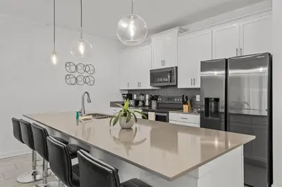 a white kitchen with a large kitchen island with black appliances at Disney Getaway Private Pool Themed Bedrooms. Book Now SLR1243 in Kissimmee
