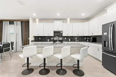 a kitchen with white cabinets and a large island with white chairs at Disney Private Pool Hot Tub Themed Bedrooms. Book Now SLR494 in Kissimmee