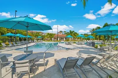 a pool with tables and chairs and blue umbrellas at Elegante Casa 3 Quartos no Vista Cay in Orlando