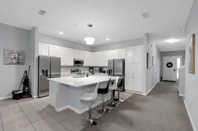 a kitchen with white cabinets and a large island with bar stools at Cozy Rooms In An Elegant House in Kissimmee