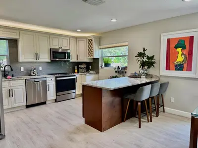 a kitchen with white cabinets and a island with bar stools at Chic & Stylish 3BR-2BA Nature Lovers Home in Orlando