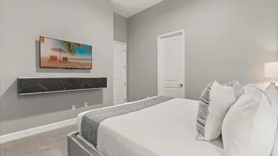 a white bedroom with a bed and a painting on the wall at Lakeside Villa with Pool BBQ Cinema & Games Room in Kissimmee