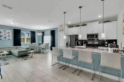 a kitchen and living room with white cabinets and a table at Heated Pool 5-Star Amenities Near Disney in Kissimmee