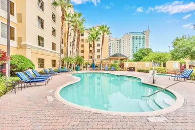 a swimming pool with chairs and palm trees and buildings at 1BR Condo w Hot Tub & Pool Close to Universal Studio in Orlando