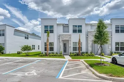 a white house with a car parked in a parking lot at Casa 4Q Hidden Forest c/ Piscina in Orlando
