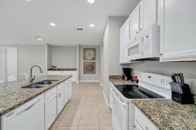a white kitchen with white appliances and marble counter tops at Spacious Fun Retreat With Private Pool And Game Room Near Disney And Waterpark & Resort Access At Encore Resorts Reunion - 7659Wi in Orlando