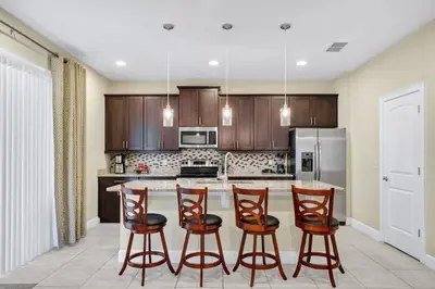 a kitchen with wooden cabinets and a island with bar stools at Home With Theme Room, Private Pool & Game Room Near Disney With Waterpark And Resort Access At Encore Resort Reunion - 471La in Orlando