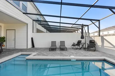a swimming pool with chairs and a table next to a house at Brand New 05 Bedrooms At Windsor Cay in Orlando