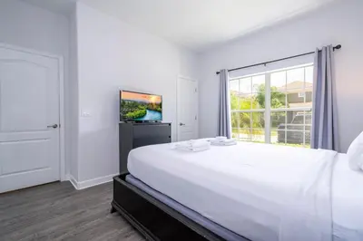 a white bedroom with a large bed and a window at Paradise Palms - Spacious house and swimming pool in Kissimmee