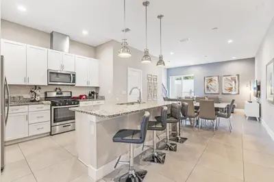 a kitchen with white cabinets and a large island with bar stools at Sunrise Shores townhouse in Orlando