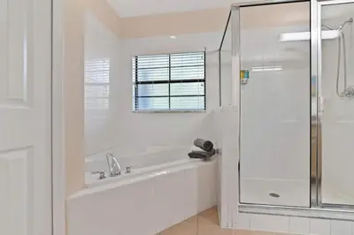 a white bathroom with a tub and a glass shower at Serene Gem, close to Disney- HEATEDsaltwaterPOOL in Kissimmee